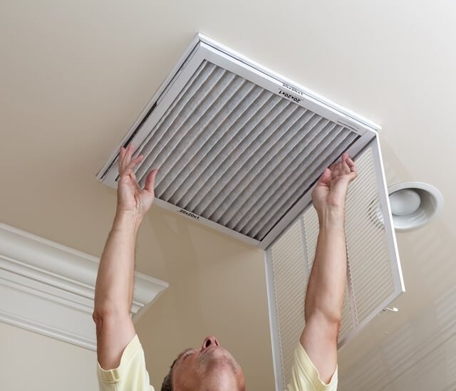 homem abrindo o filtro de ar-condicionado no teto